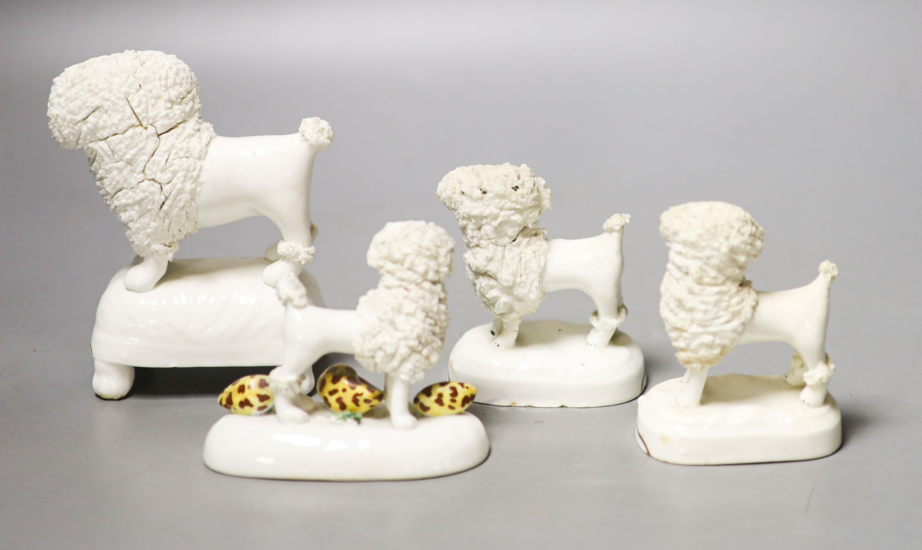 Four Staffordshire porcelain figures of poodles holding a basket of flowers, c.1830-50, one modelled with shells to the base 12cm